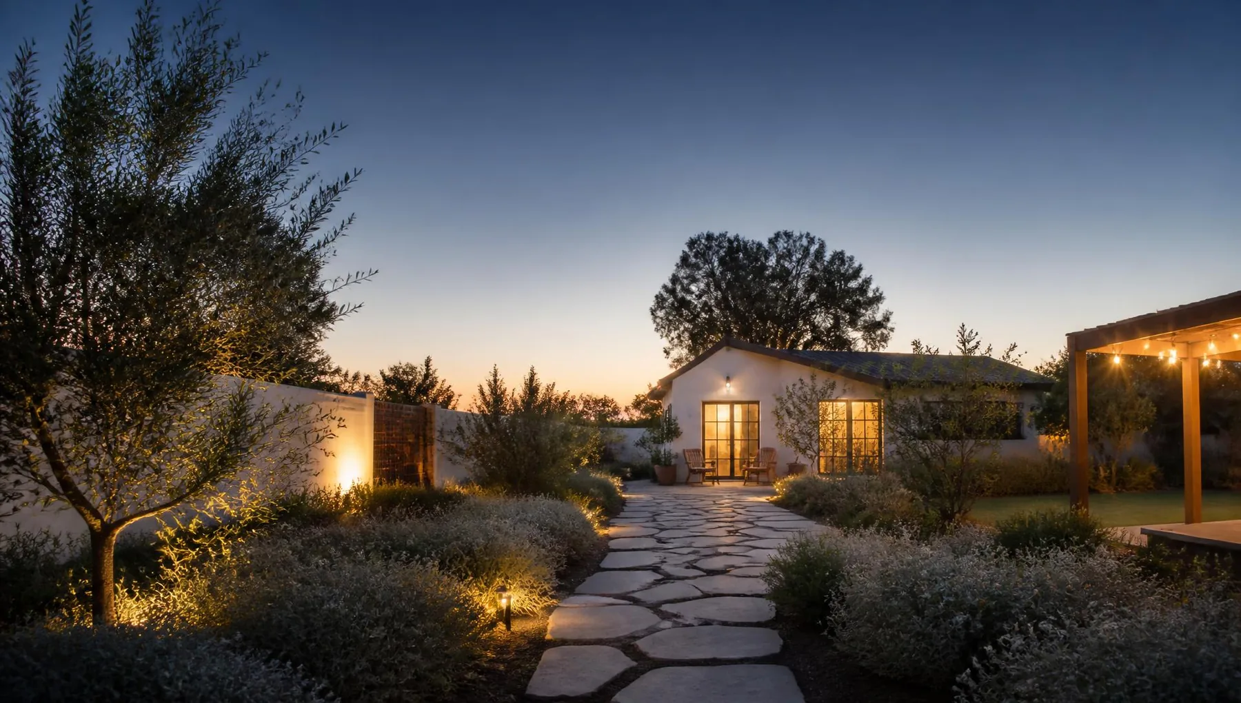 Twilight view of a finished backyard with a warm-lit studio at the end of a stone path